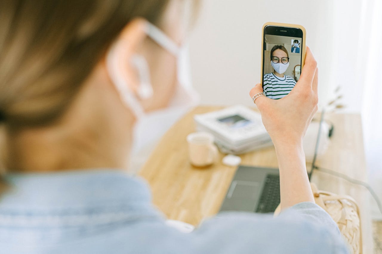 Woman wearing face mask making a video call on smartphone in cozy home setting.